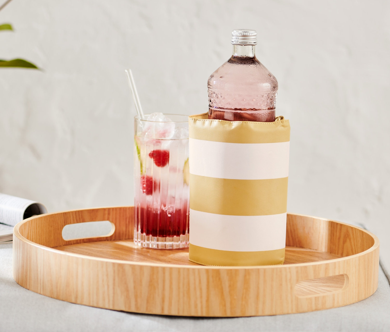 Auf einem Holztablett stehen ein Getränkeglas und eine Flaschen-Kühlmanschette mit einer Flasche.