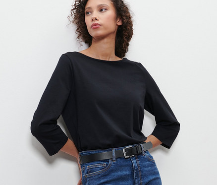 Frau lehnt an Wand, trägt Jeans und Ledergürtel.