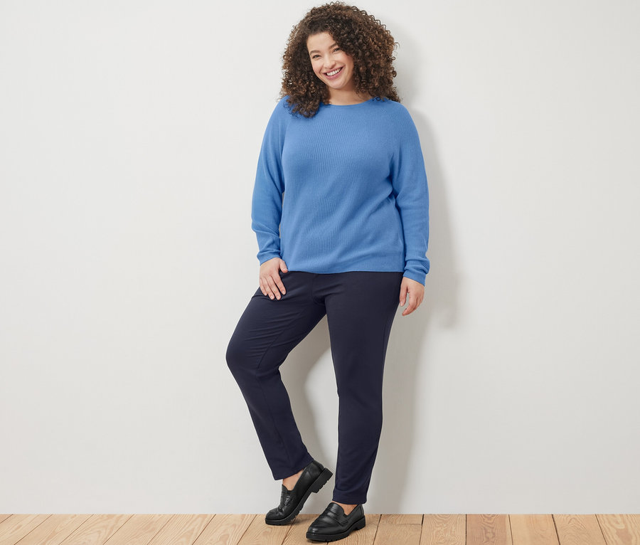 Frau posiert in blauem Strickpullover und marineblauer Joggpants.