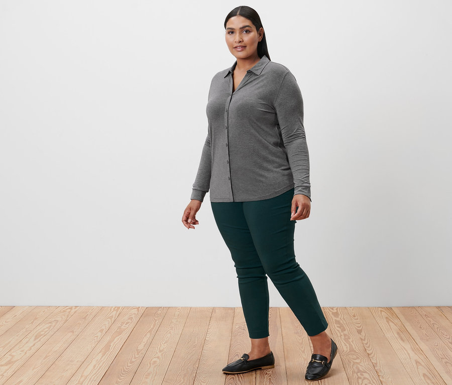 Frau geht, trägt ein grau meliertes Blusenshirt mit Knopfleiste, eine Stretchhose und Leder-Loafer.