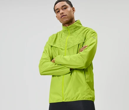 Mann mit verschränkten Armen trägt neonlime Windprotection-Laufjacke.