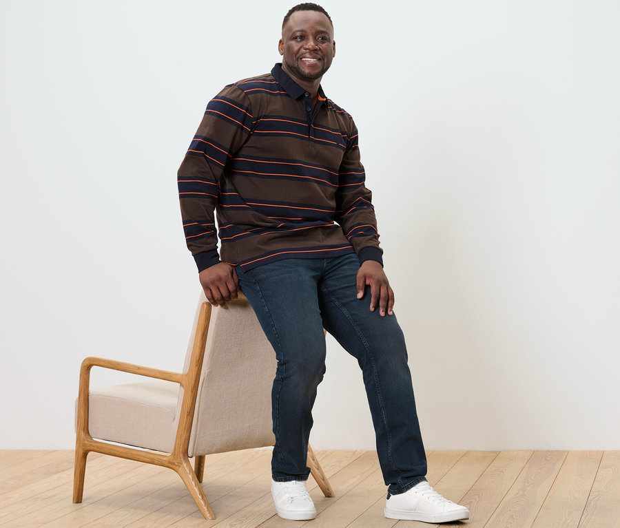 Mann sitzt auf einem Stuhl und trägt ein Langarm-Poloshirt.