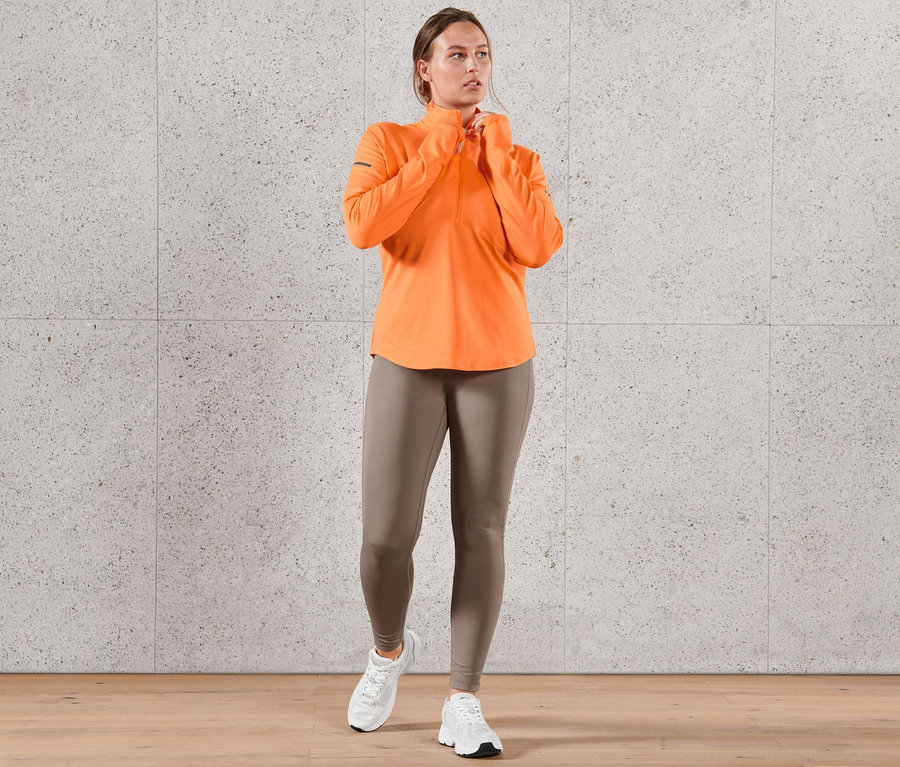 Frau trägt ein neonorangefarbenes Thermo-Funktionsshirt und eine Sporttight.