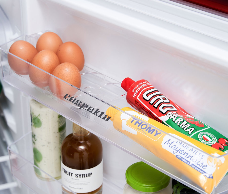 Innenraum eines Kühlschranks mit Eiern, Soßen und Getränken in durchsichtigen Plastikbehältern. Zu sehen ist eine Respekta Kühl-Gefrierkombination »KS144VC«, Vintage Cream.