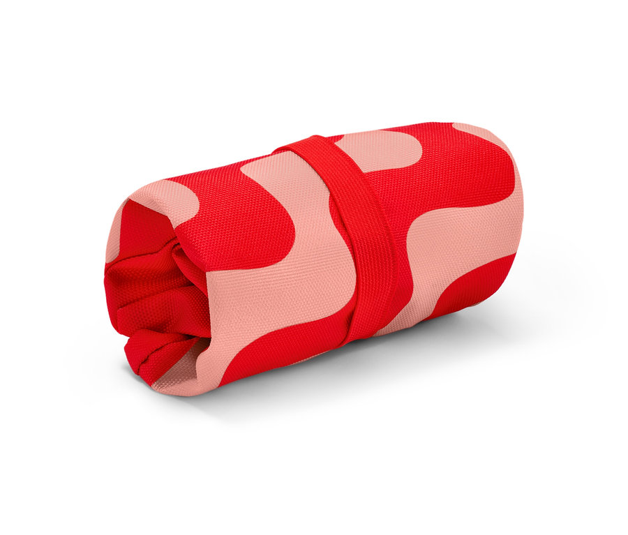 Ein aufgerollter Fahrradsattelbezug mit rotem Muster auf rosa Hintergrund.