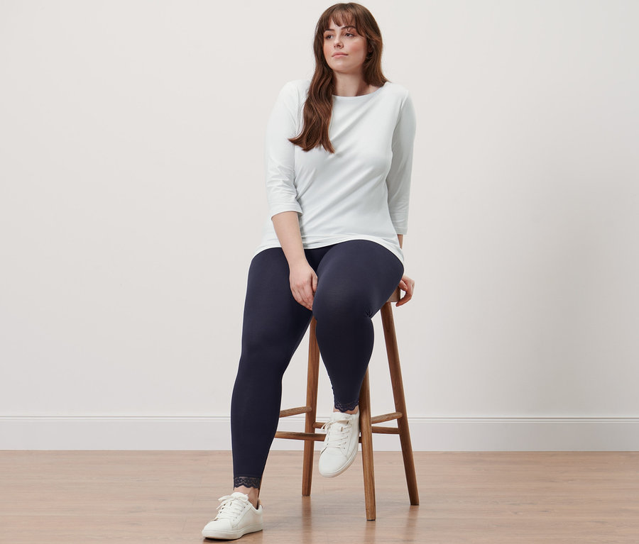 Frau sitzt auf einem Hocker, trägt ein Shirt mit 3/4-Arm und Leggings mit Spitzenborte.