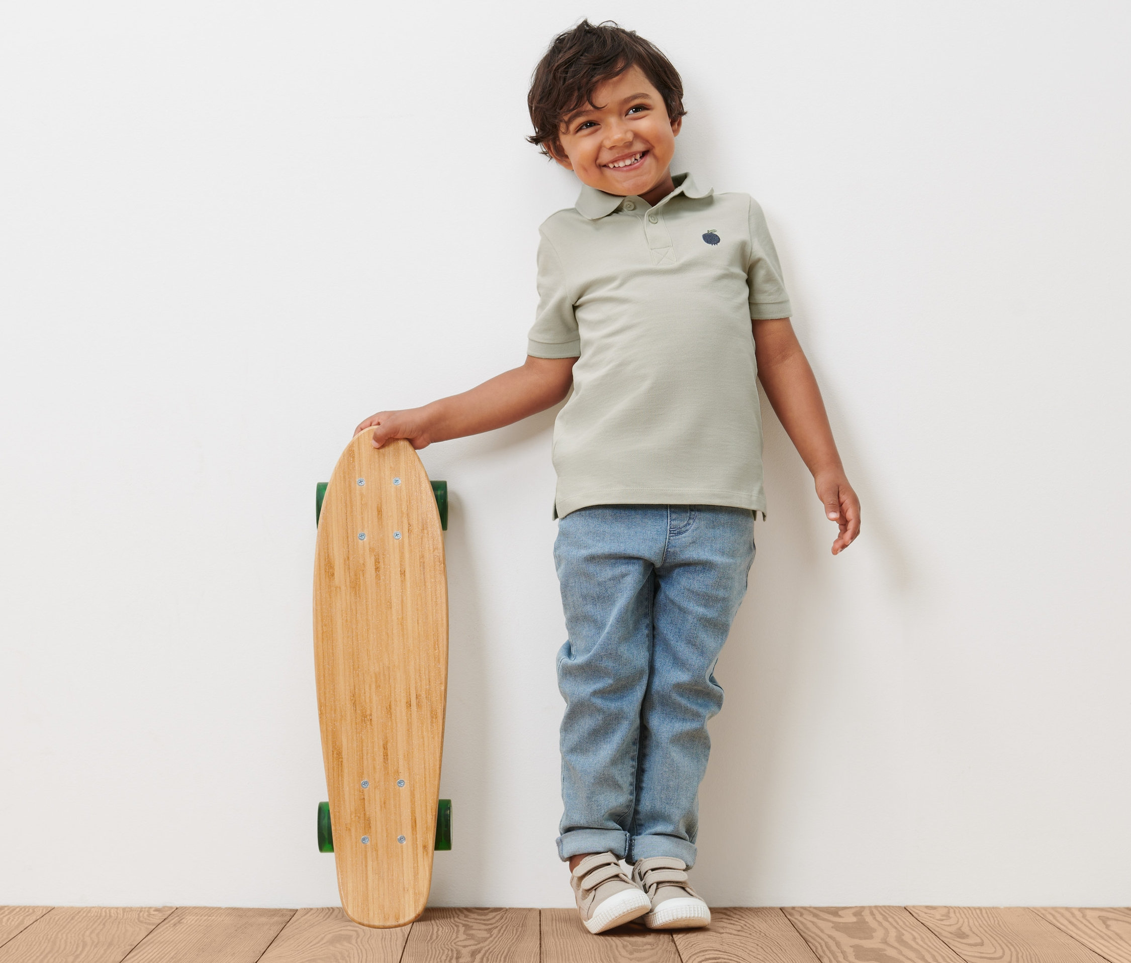 Junge lehnt mit 2 Kleinkind-Poloshirts an einem Skateboard.
