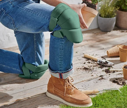 Eine Person kniet mit Garten-Knieschonern und hält einen Topf mit einer Pflanze.