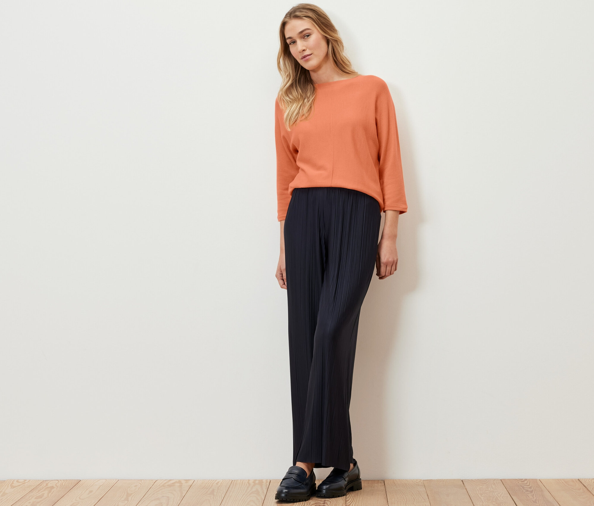 Frau steht und trägt einen peachfarbenen Merino-Feinstrickpullover.