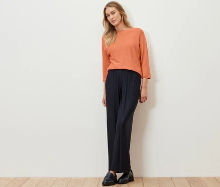 Frau steht und trägt einen peachfarbenen Merino-Feinstrickpullover.