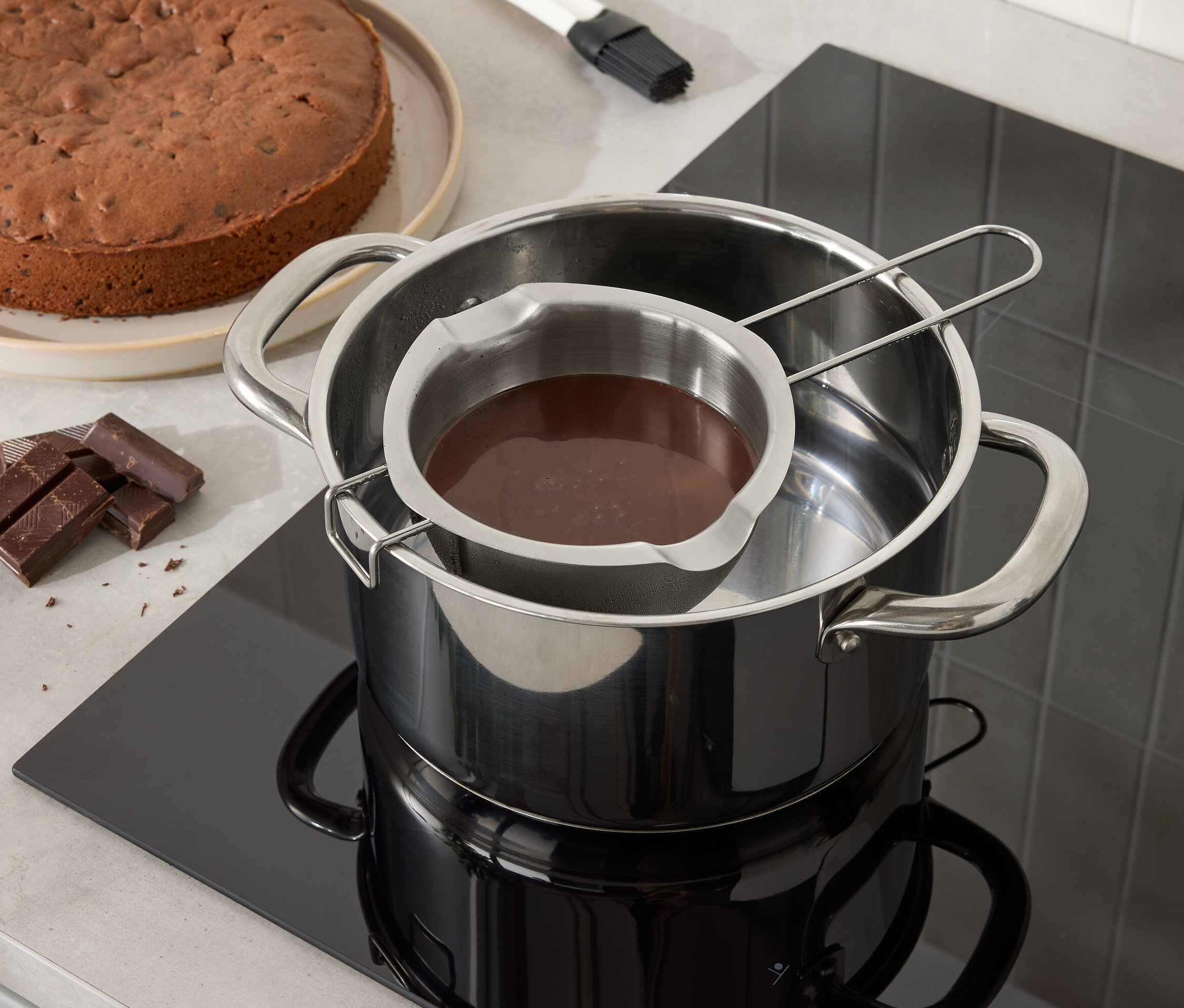 Schokoladenkuchen und Schokolade schmelzen in einer Edelstahlschüssel über einem Topf mit Wasser.