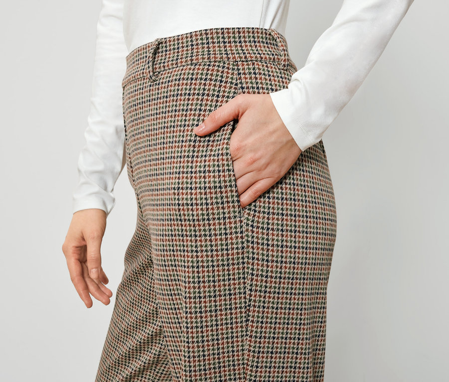 Eine Frau hat ihre Hand in der Tasche einer braun karierten Hose.