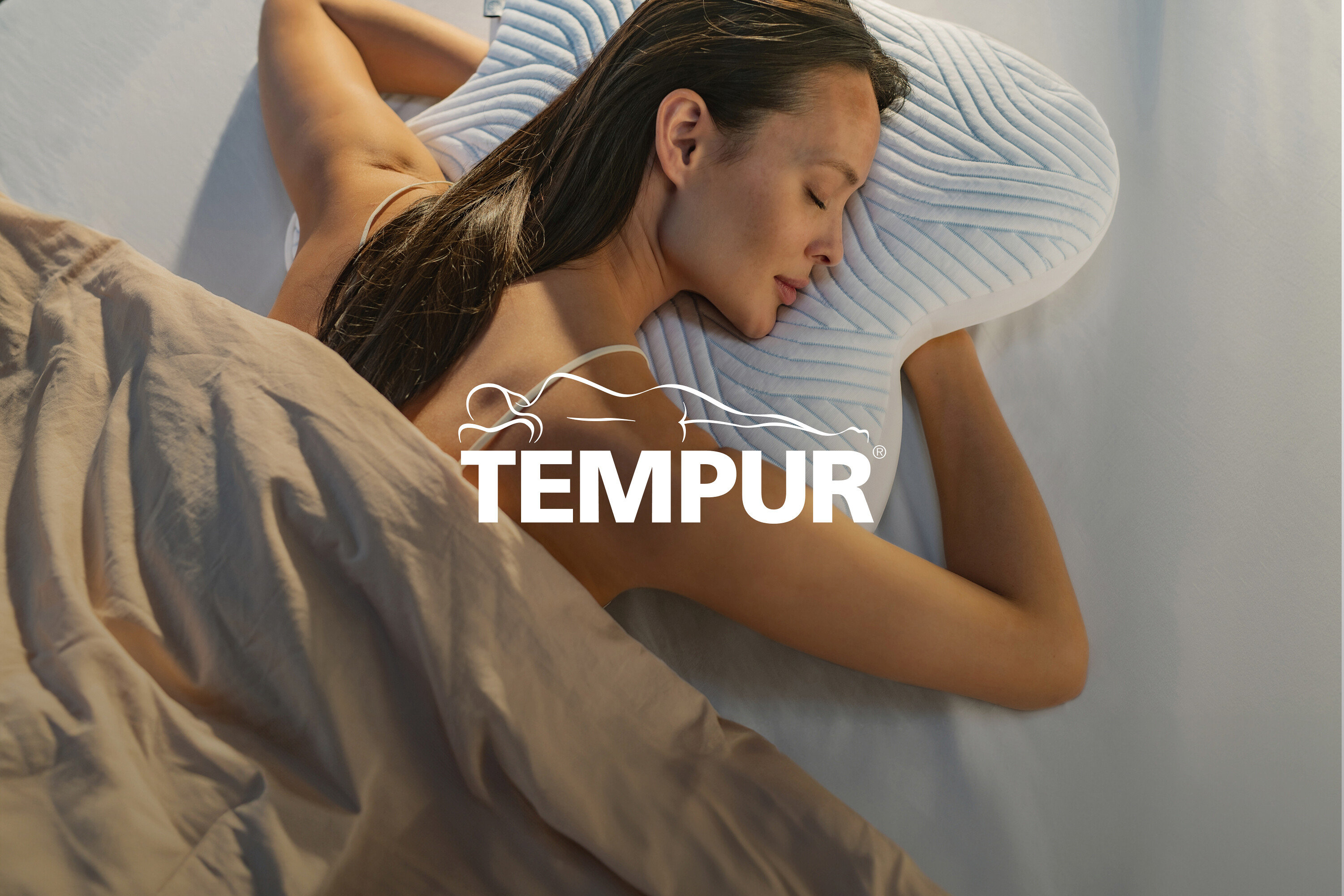 Frau liegt mit geschlossenen Augen auf einem hellblauen Kissen unter einer beigen Decke.