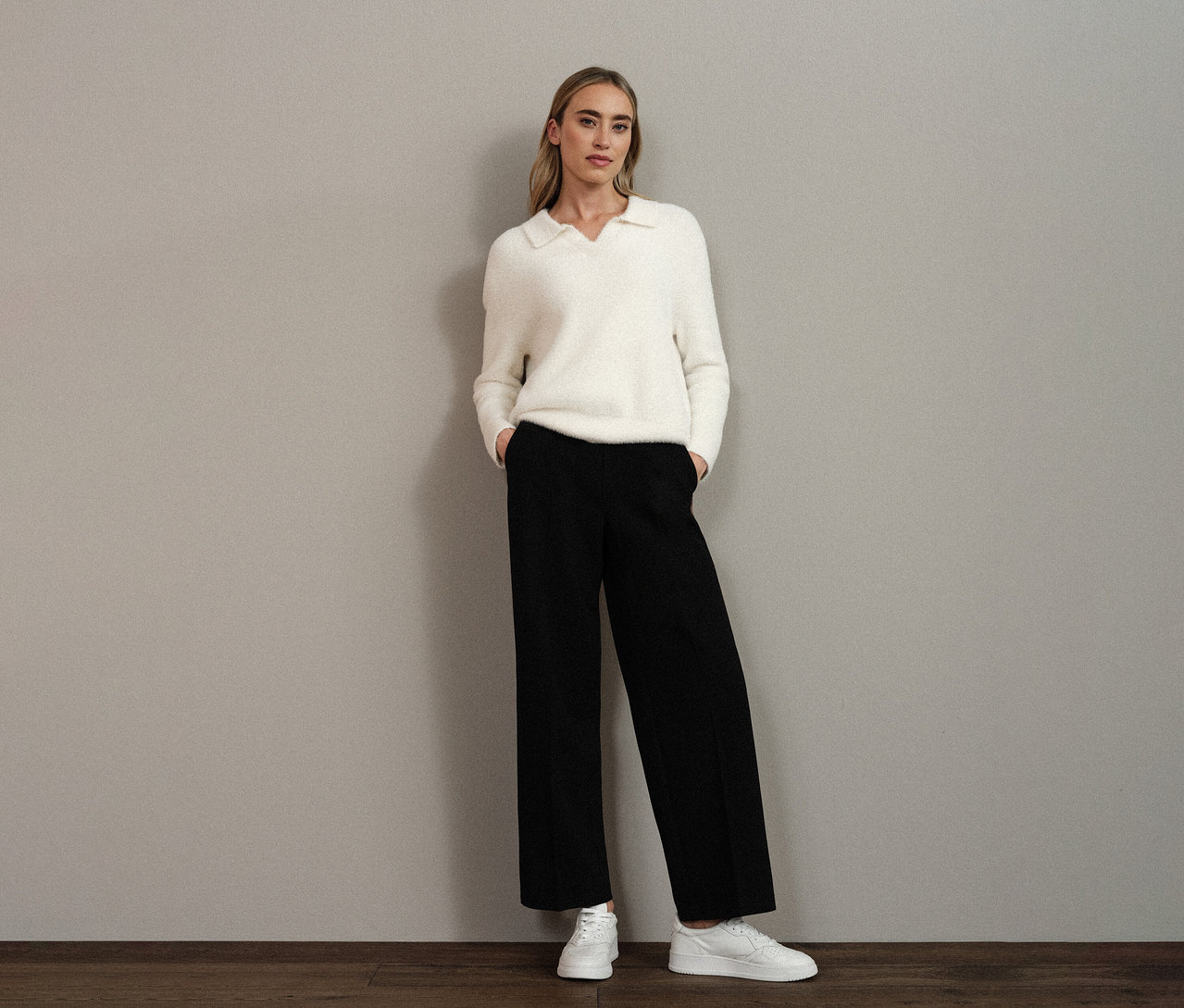 Frau mit einem weißen Street One Strickpullover mit Polokragen, schwarzer Hose und weißen Schuhen.