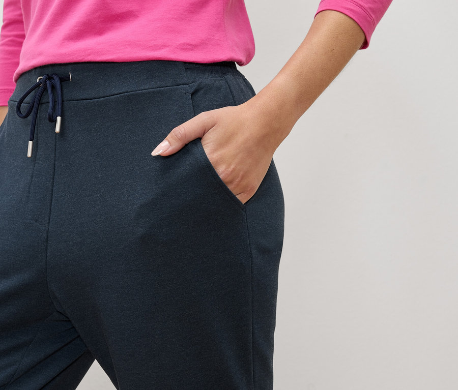 Nahaufnahme einer Person, die marineblaue Jogginghose mit Kordelzug und Taschen trägt und eine Hand in der Tasche hat.