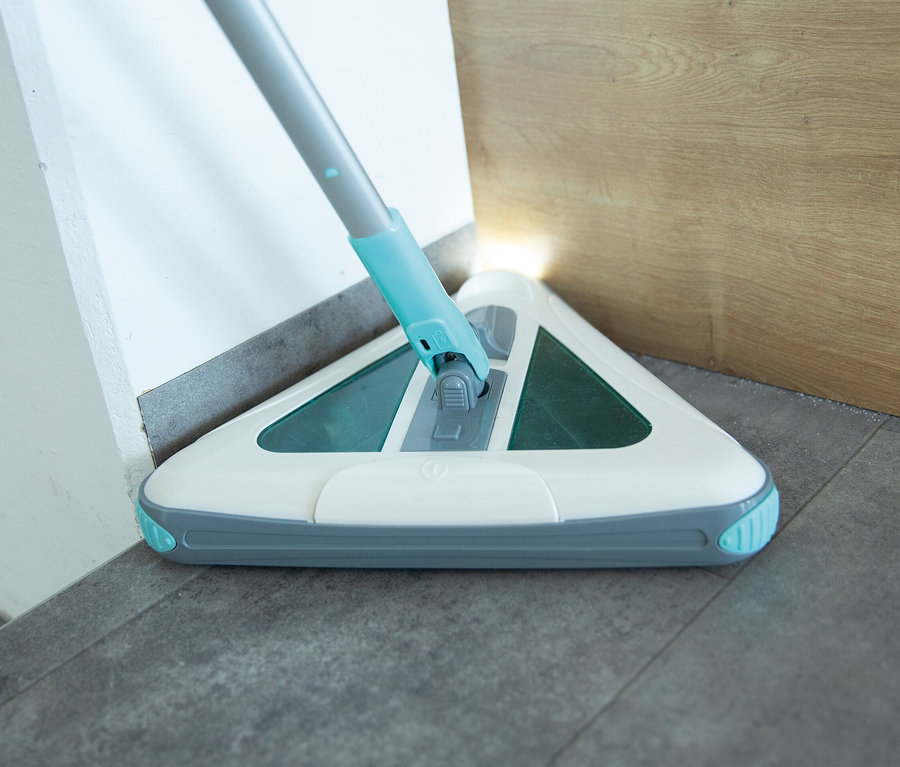 Ein Akkubesen reinigt eine Ecke des Zimmers.