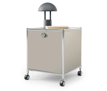 Auf der Oberseite eines beigen Rollcontainers stehen eine graue Lampe und ein Buch.