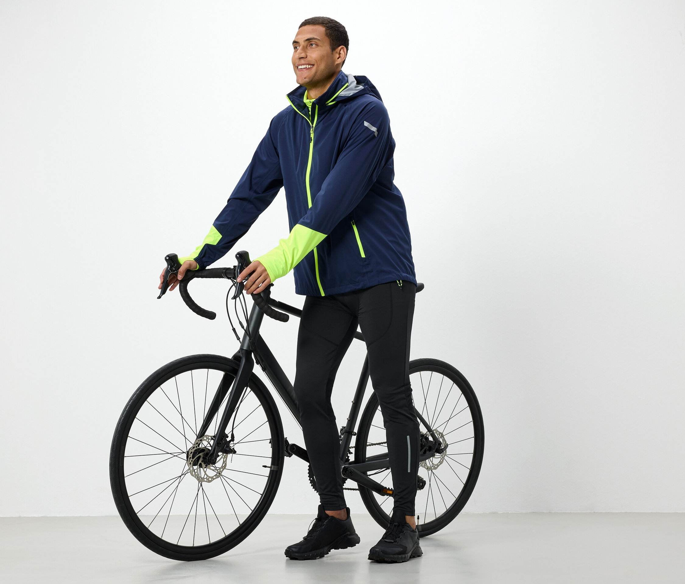 Mann in Jacke hält ein schwarzes Fahrrad.