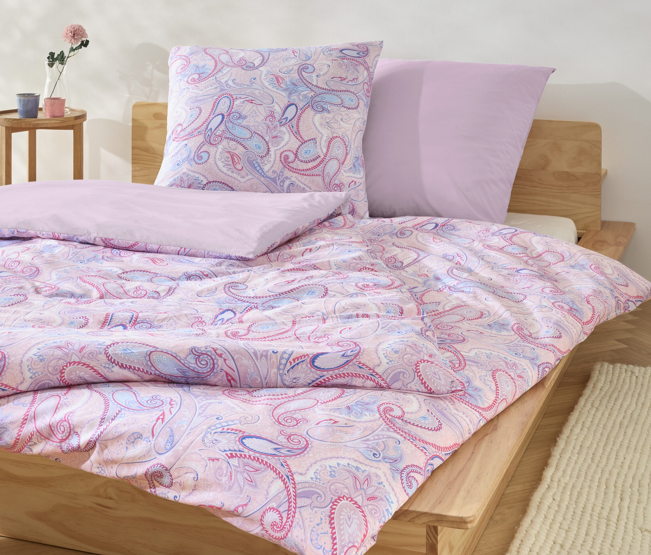Auf einem Bett liegt rosafarbene Renforcé-Bettwäsche mit Paisley-Muster, darunter drei Sets in Normalgröße und ein Set in Übergröße.