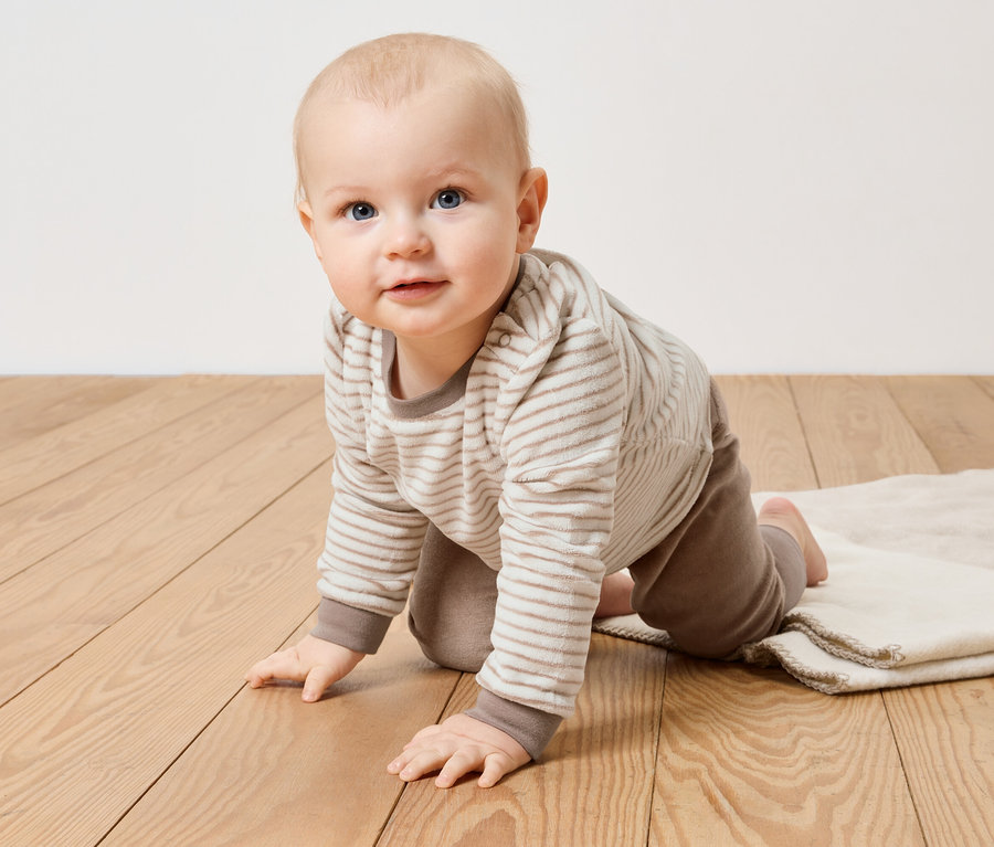 Ein Baby krabbelt in einem Nicki-Set auf einem Holzboden.