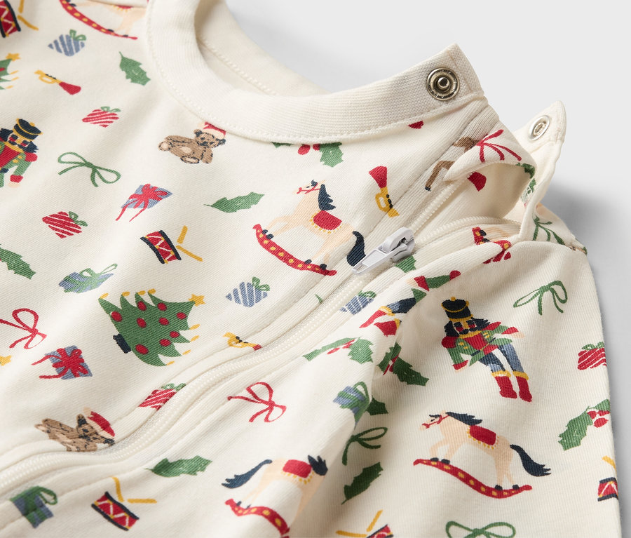 Detailaufnahme eines Baby-Schlafanzugs mit Weihnachtsmotiven, Reißverschluss und Druckknöpfen.