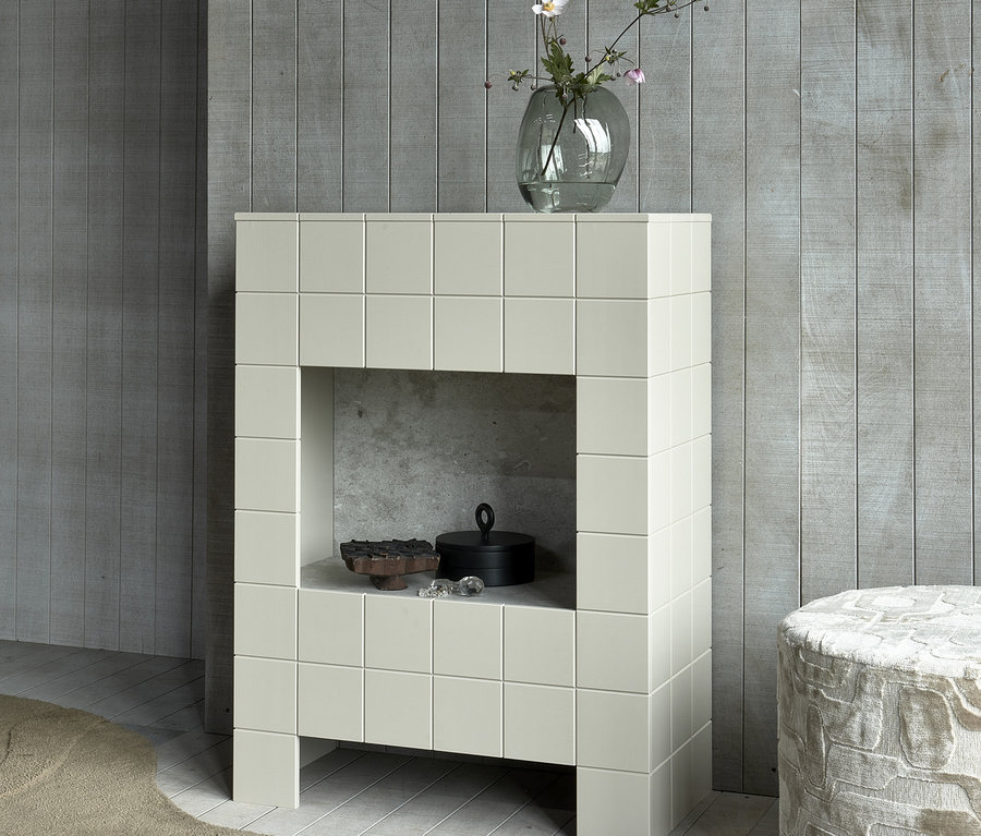 Ein beiger Schrank mit Fliesendekor und einer Öffnung, in der sich ein schwarzes Gefäß und eine Dekoration befinden, daneben ein beiger Hocker und eine Vase mit Blumen. Woood Hocker »Yago«, naturfarben, 60 x 43 cm
