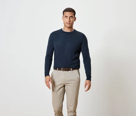 Mann steht und trägt einen dunkelblauen Pullover, einen braunen Gürtel und Khakihosen.