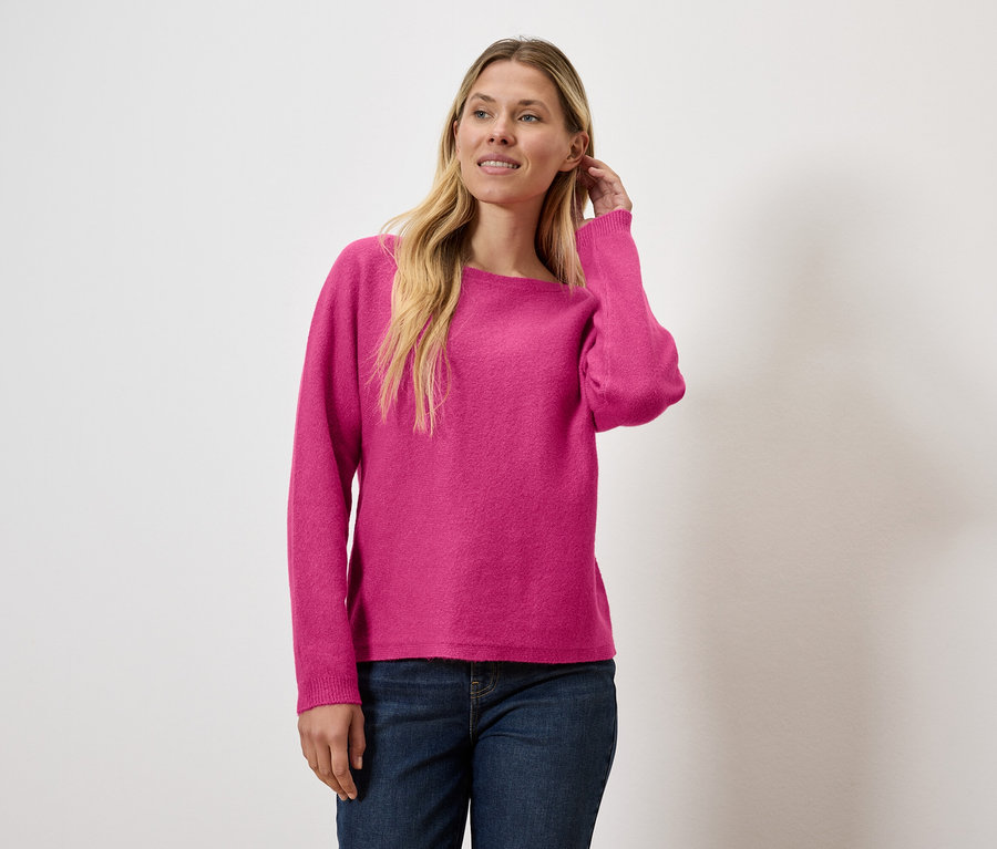 Frau ordnet ihr Haar, trägt einen pinken Pullover und Jeans.