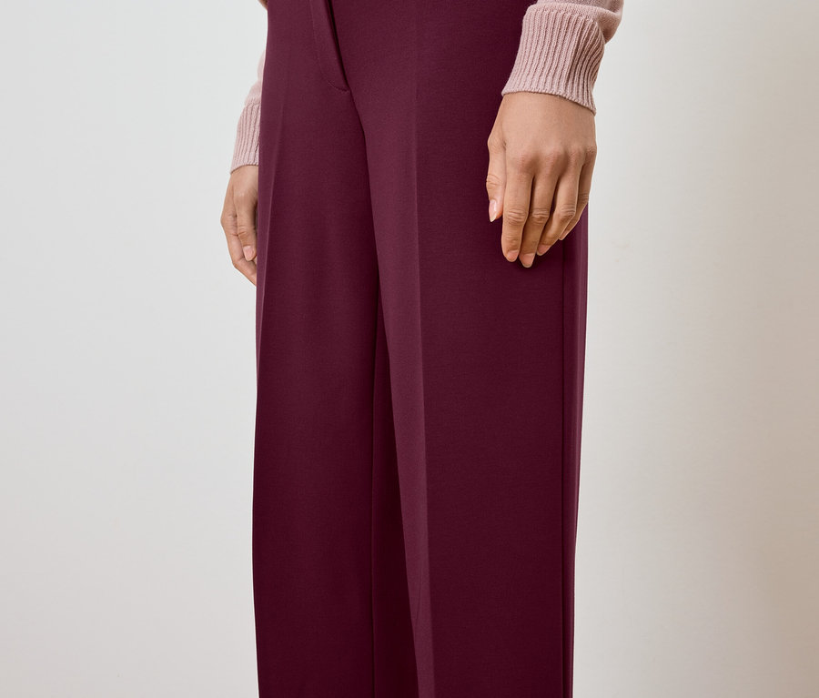 Teilansicht einer Person, die eine weinrote Hose und einen hellrosa Pullover trägt.