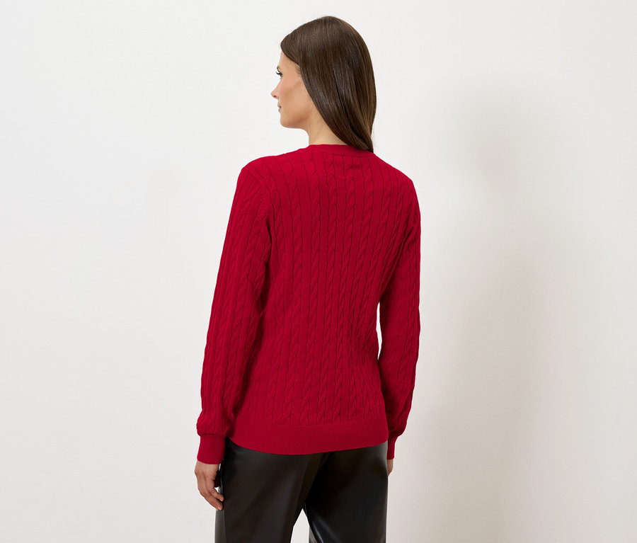 Frau steht mit dem Rücken zur Kamera und trägt einen roten Pullover und eine schwarze Lederhose.