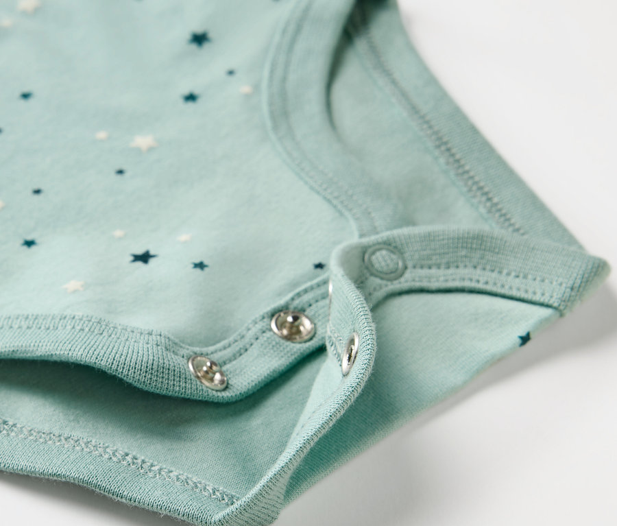 Detailaufnahme eines hellblauen Babybodys mit Sternenmuster und Druckknöpfen.