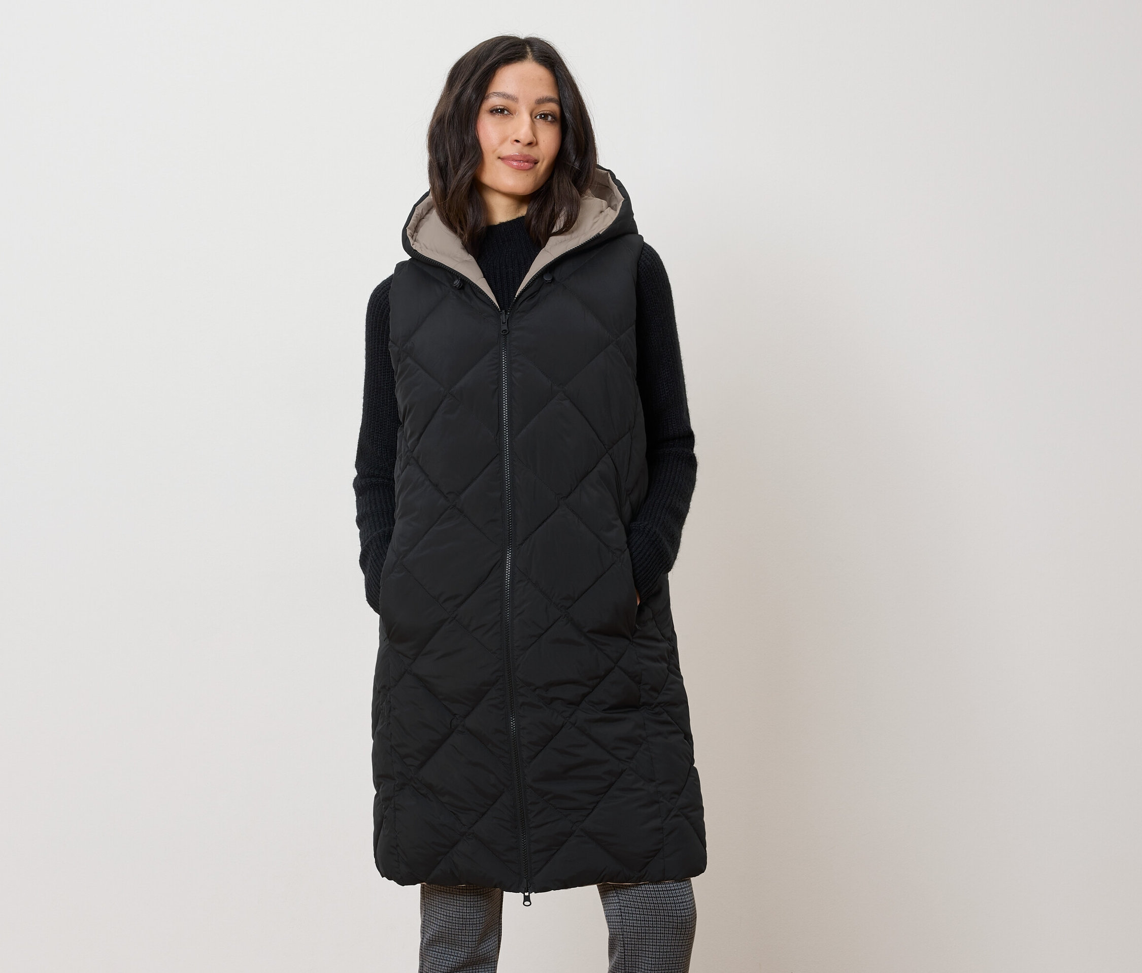 Eine Frau trägt eine lange, gesteppte, schwarze Weste mit Kapuze.