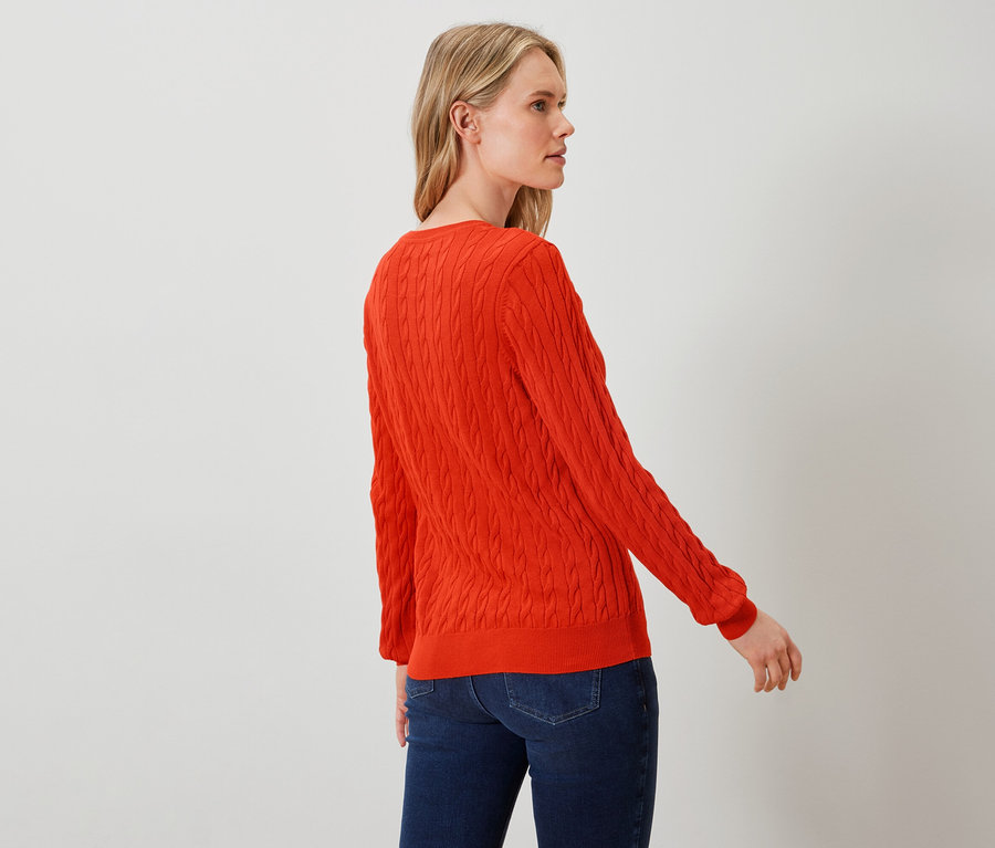 Eine Frau posiert in einem orangefarbenen Pullover und blauen Jeans.