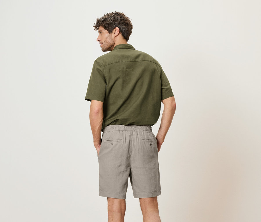 Ein Mann von hinten, trägt ein grünes Hemd und graue Shorts.