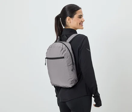 Frau mit Pferdeschwanz trägt grauen Rucksack und schwarze Sportbekleidung, Blick von der Seite.
