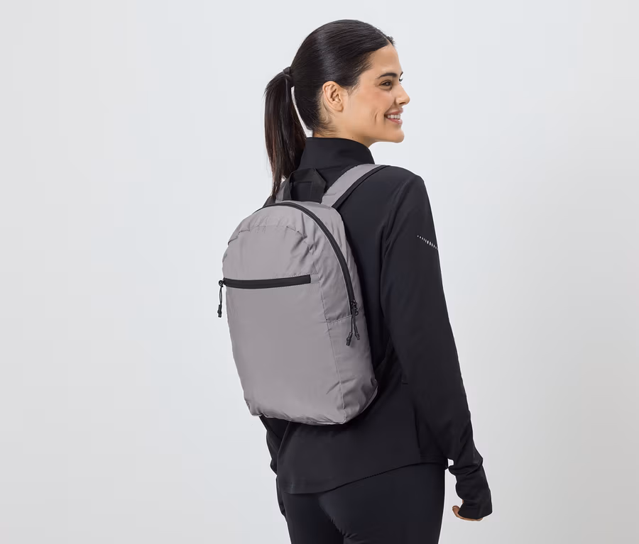 Frau mit Pferdeschwanz trägt grauen Rucksack und schwarze Sportbekleidung, Blick von der Seite.