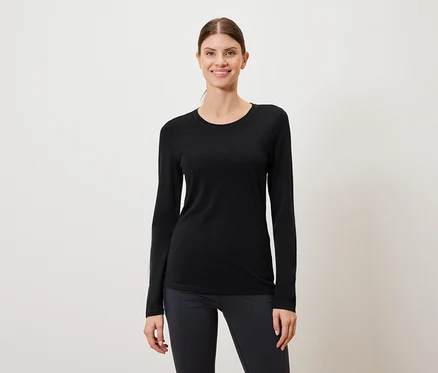 Frau trägt ein schwarzes Langarmshirt und dunkle Leggings vor einem weißen Hintergrund.