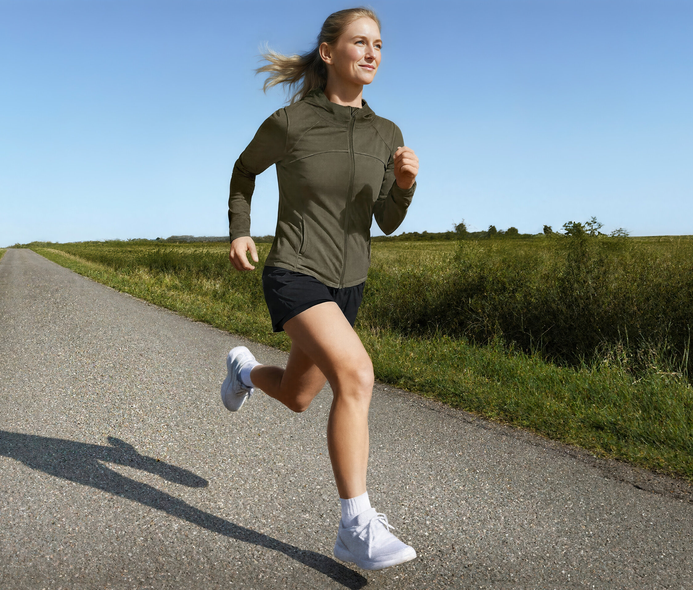 Frau läuft in Sportjacke und 2-in-1-Laufshorts auf einer Landstraße.