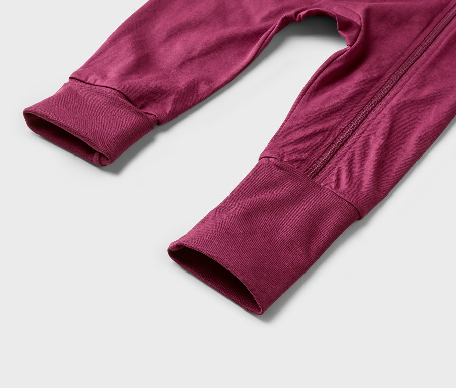 Nahaufnahme von Ärmeln und Hosenbeinen eines bordeauxroten Overalls mit Reißverschluss.