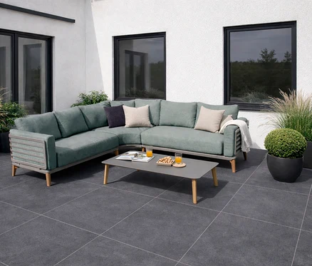 Salbeigrüne Leco Lounge-Ecke »Moss« mit Tisch auf einer Terrasse vor einem weißen Haus mit Fenstern und Pflanzen.