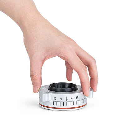 Eine Hand dreht an einem silberfarbenen Ring mit schwarzem Innenleben und rotem Akzent, der mit "C" und "F" beschriftet ist.