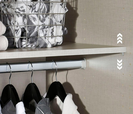 Einblick in einen Kleiderschrank mit einer Ablage, einem Drahtkorb mit Textilien und Kleidung an Kleiderbügeln an einer Stange.