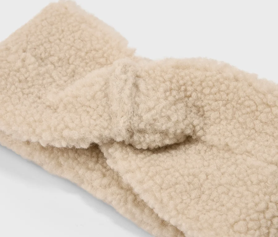 Nahaufnahme eines beigen, verdrehten Stirnbandes aus Teddyplüsch.