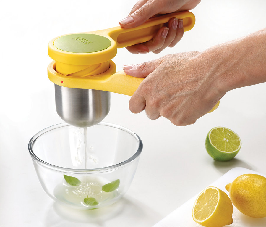 Hände pressen mit einem gelben Joseph Joseph Pressen-Set, 3-teilig, Saft in eine Schüssel.