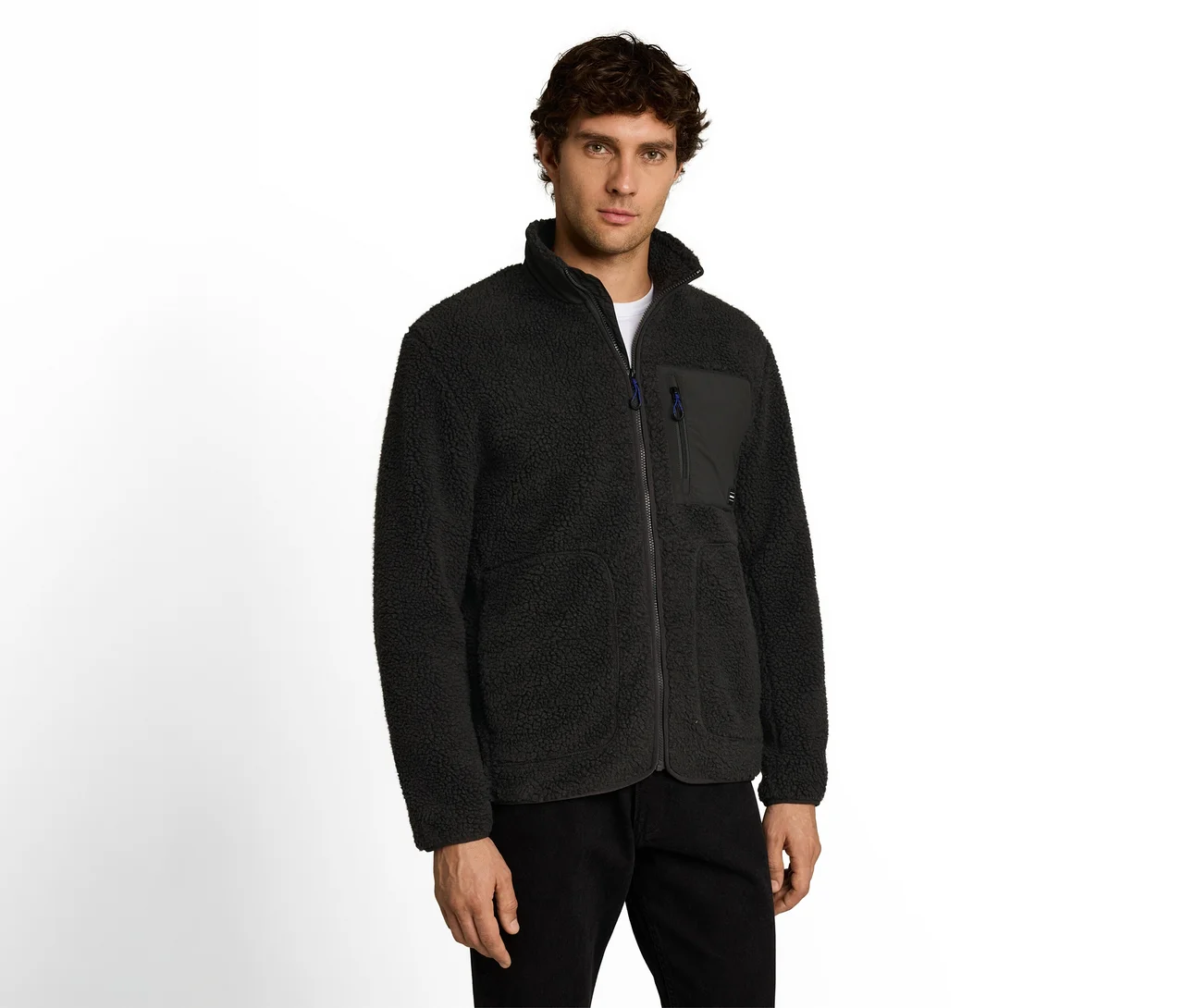 Mann trägt eine schwarze Fleecejacke mit Stehkragen und Brusttasche sowie eine schwarze Hose und blickt nach vorne.