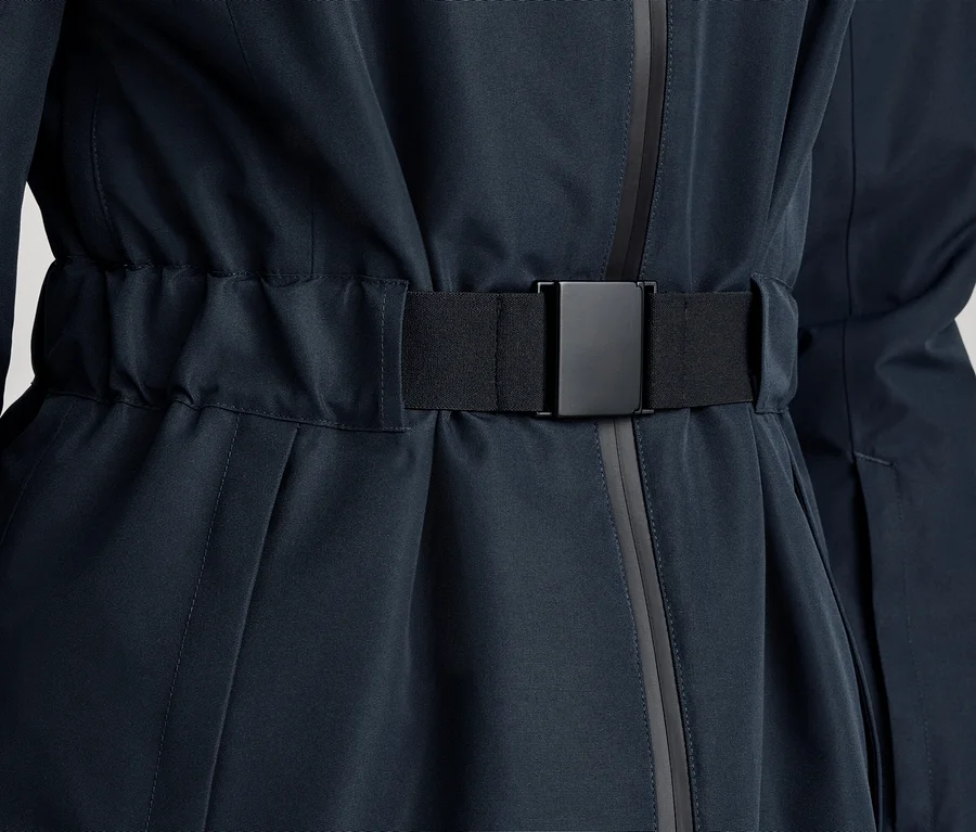 Nahaufnahme einer dunkelblauen Jacke oder eines Mantels mit einem schwarzen, elastischen Gürtel und einer schwarzen, rechteckigen Schnalle, die die Taille rafft.