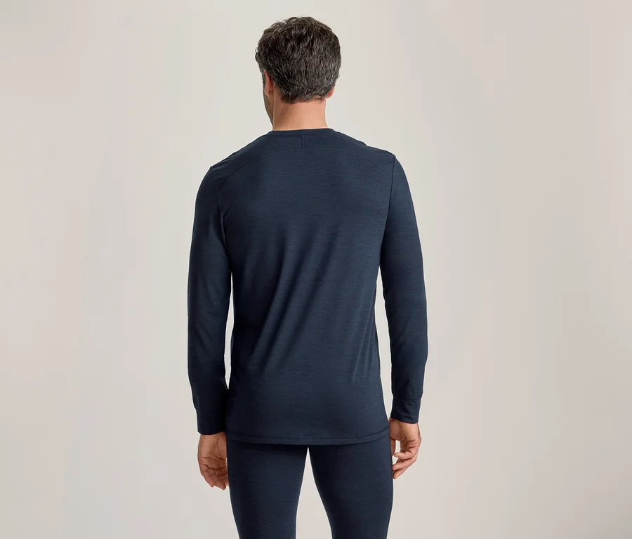 Mann von hinten in einem dunkelblauen Langarmshirt und passender langer Hose vor schlichtem Hintergrund.