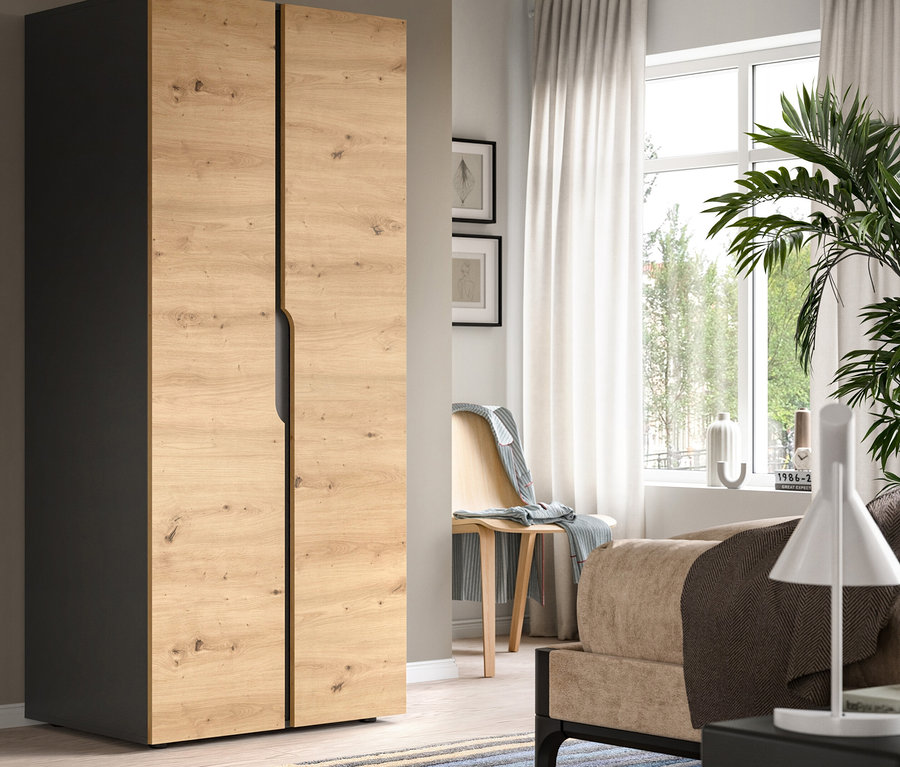 Modernes Schlafzimmer mit einem zweitürigen Kleiderschrank, links dunkelgrau und vorne helles Holzdekor. Ein gestreifter Teppich liegt am Boden, und ein Fenster mit weißen Vorhängen ist im Hintergrund, neben einem Holzstuhl mit einer Decke.
