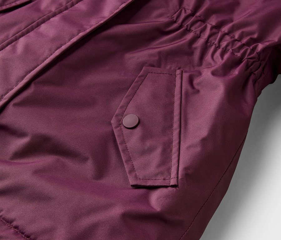 Nahaufnahme einer bordeauxroten Jacke mit einer Pattentasche mit Druckknopf und einem elastischen Detail an der Seite.