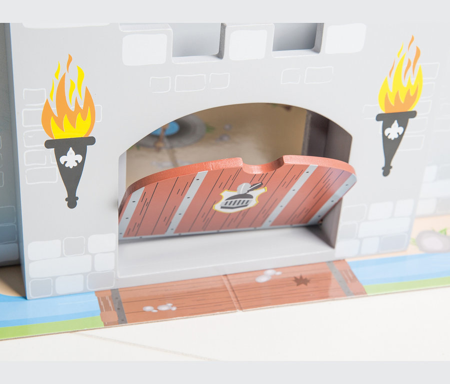 Nahaufnahme einer grauen Spielzeugburg mit Torbogen. Eine braune Zugbrücke mit Wappen ist teilweise geöffnet. Zwei gemalte Fackeln mit Flammen flankieren den Torbogen. Eine bedruckte Matte mit Brücken- und Wassergraben-Design liegt am Fuß.
